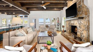 A spacious living room with a stone fireplace, a flat-screen TV mounted on the wall, and a ceiling fan.