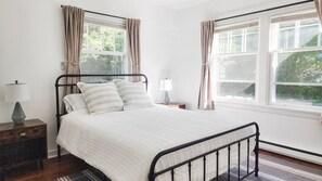 A bedroom with a bed, two bedside tables, a lamp, and a window with curtains.