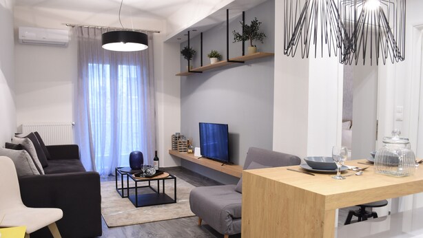 Ein modernes Wohnzimmer mit einer Couch, einem Couchtisch, einem Fernseher und einem Essbereich mit Tisch und Stühlen.