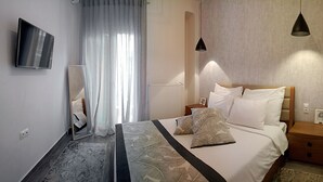 Ein modernes Hotelzimmer mit einem großen Bett, einem Nachttisch, einem Wand-Fernseher und einem Fenster mit transparenten Vorhängen.