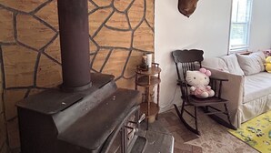A rustic interior with a wood-burning stove, a stone wall, a mounted deer head, a rocking chair, and a Hello Kitty chair. - Fabulous 2-bedroom cottage in Wurtsboro (Wurtsboro)
