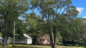A residential area with two houses, one with a porch and a red chair, surrounded by trees and a clear blue sky. - Fabulous 2-bedroom cottage in Wurtsboro (Wurtsboro)