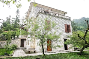 Ein Steinhaus mit Balkon, einer Tür und einem kleinen Garten mit einer Bank.