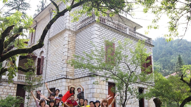 A group of people sitting on a blanket in front of a stone building with a balcony. - Khach San Cong Doan Sapa (Sa Pa)
