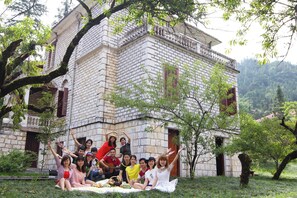 Eine Gruppe von Menschen sitzt auf einer Decke vor einem Steinhaus mit einem Balkon.