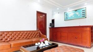 A room with a brown leather sofa, a wooden coffee table with a flower vase, a wooden reception desk, and a world map on the wall. - Khach San Cong Doan Sapa (Sa Pa)
