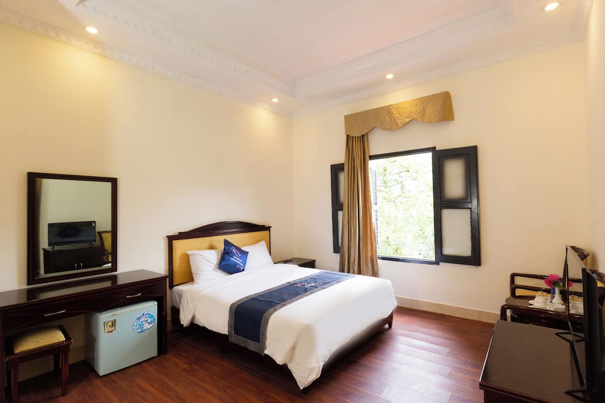 A hotel room with a bed, a desk, a chair, a small refrigerator, a television, and a window with curtains.