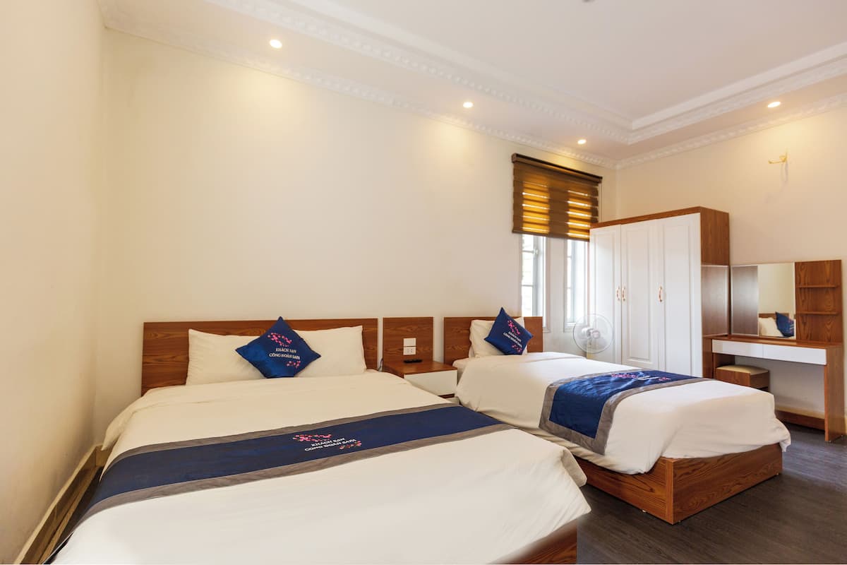 A hotel room with two beds, a wooden wardrobe, a bedside table, and a mirror.