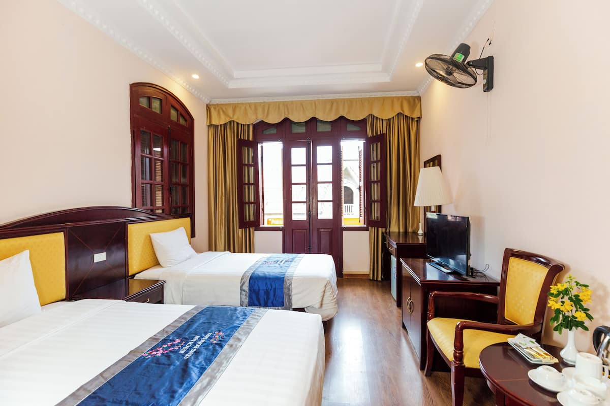 A hotel room with two beds, a desk with a television, a chair, and a window with curtains.