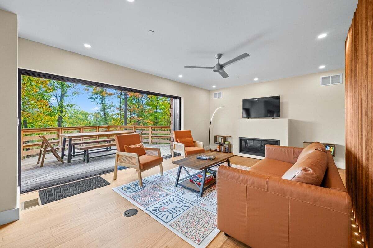 Un salon moderne doté d’une grande fenêtre, d’un ventilateur de plafond, d’une cheminée et d’un téléviseur fixé au mur.