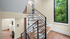 Un interior moderno con una escalera en espiral, un ventanal con vistas a un bosque y suelo de madera.