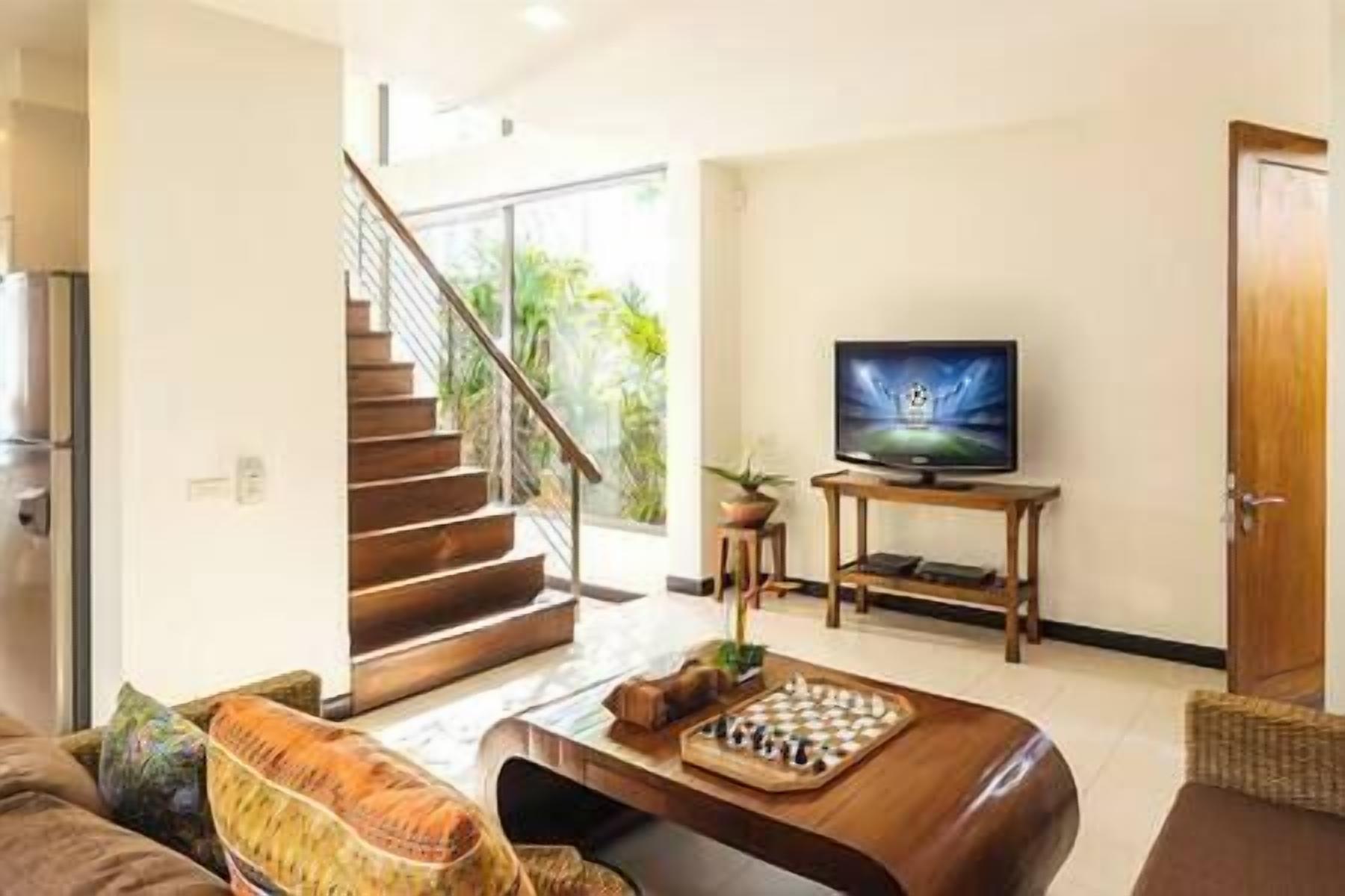Una sala de estar con una escalera de madera, un televisor y un tablero de ajedrez sobre una mesa auxiliar.