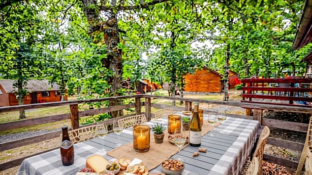 An outdoor dining area with a checkered tablecloth, a bottle of wine, glasses, cheese, and nuts.