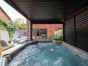 Een hottubgedeelte met een bakstenen muur, een glazen deur naar een kamer en een houten plafond.