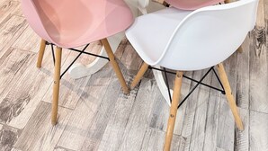 Un tavolo rotondo bianco con un vaso bianco e una pianta verde, circondato da sedie rosa e bianche dalle gambe in legno.