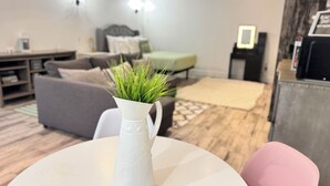 Un soggiorno con un vaso bianco pieno di piante verdi su un tavolino rotondo, un divano grigio, un poggiapiedi verde e un tappeto decorato.