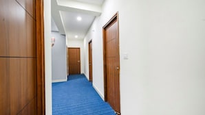 A hallway with wooden doors, a blue carpet, and white walls. - Hotel Maski Suites (Hyderabad)