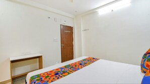 A bedroom with a bed, a wooden wardrobe, a small desk, and a white wall. - Hotel Maski Suites (Hyderabad)