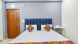 A room with a bed, two pillows, a wooden door, a white table, and a blue headboard. - Hotel Maski Suites (Hyderabad)