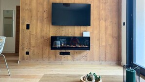 Ett modernt vardagsrum med en träpanel på väggen, en platt-TV som hänger ovanför en öppen spis och en klocka på väggen.