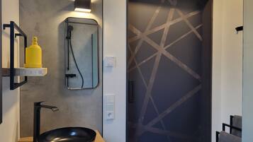 Un baño moderno con un lavabo negro, un espejo, una lámpara empotrada en la pared y una puerta con motivo geométrico.