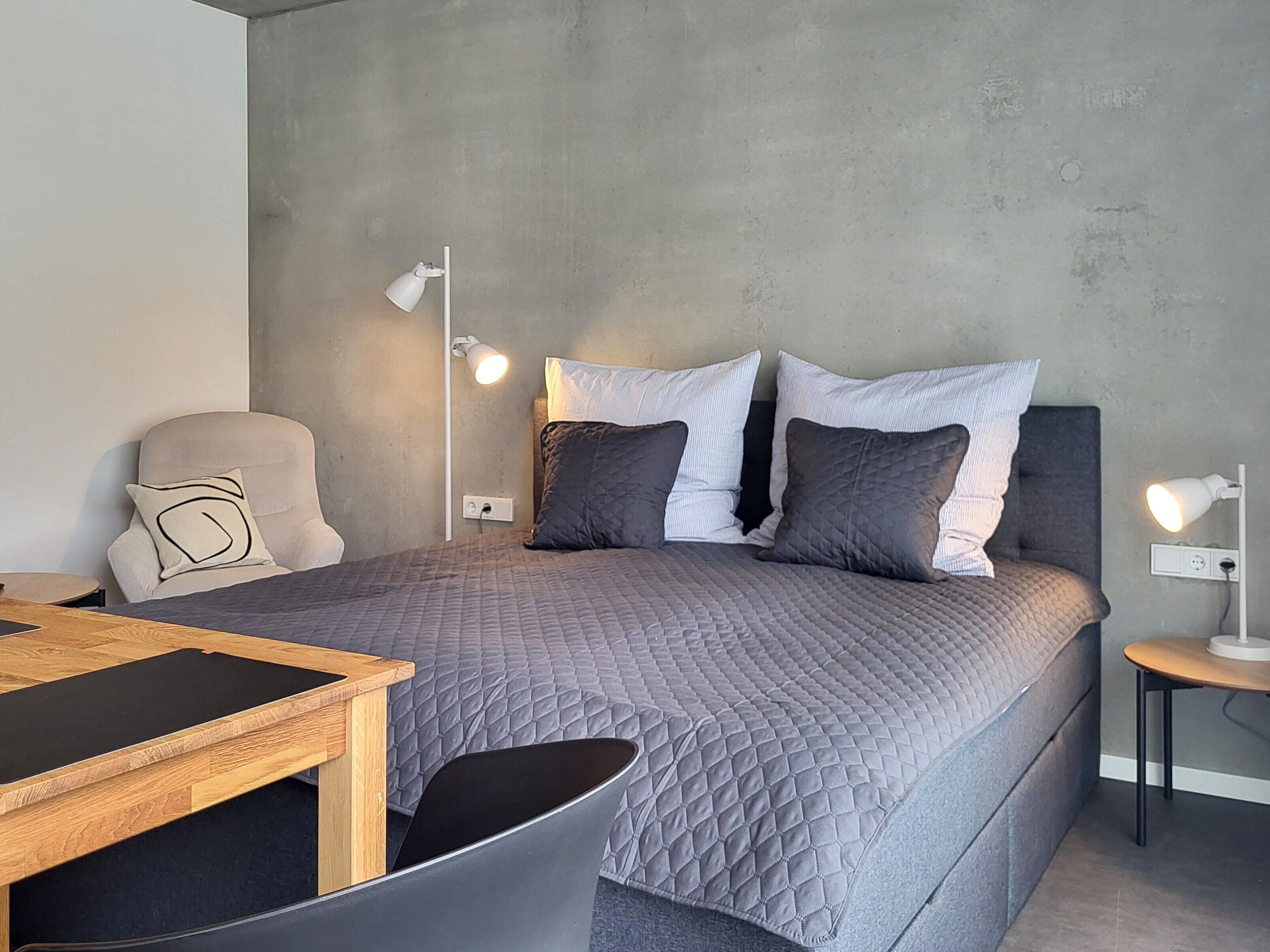 Une chambre moderne avec un lit, des lampes de chevet, une chaise et une petite table.