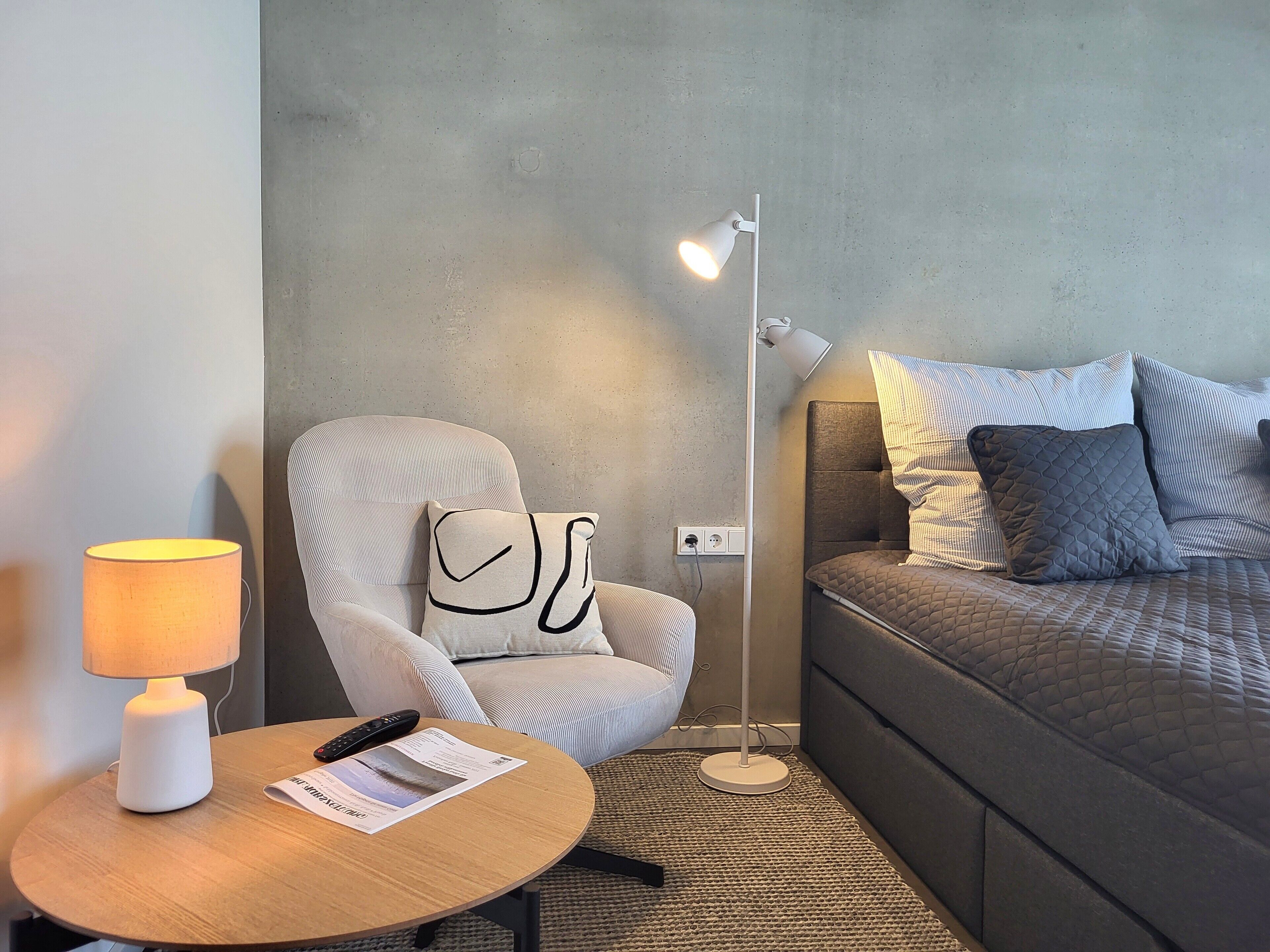 Una habitación moderna con cama, sillón, mesa y lámpara de pie.