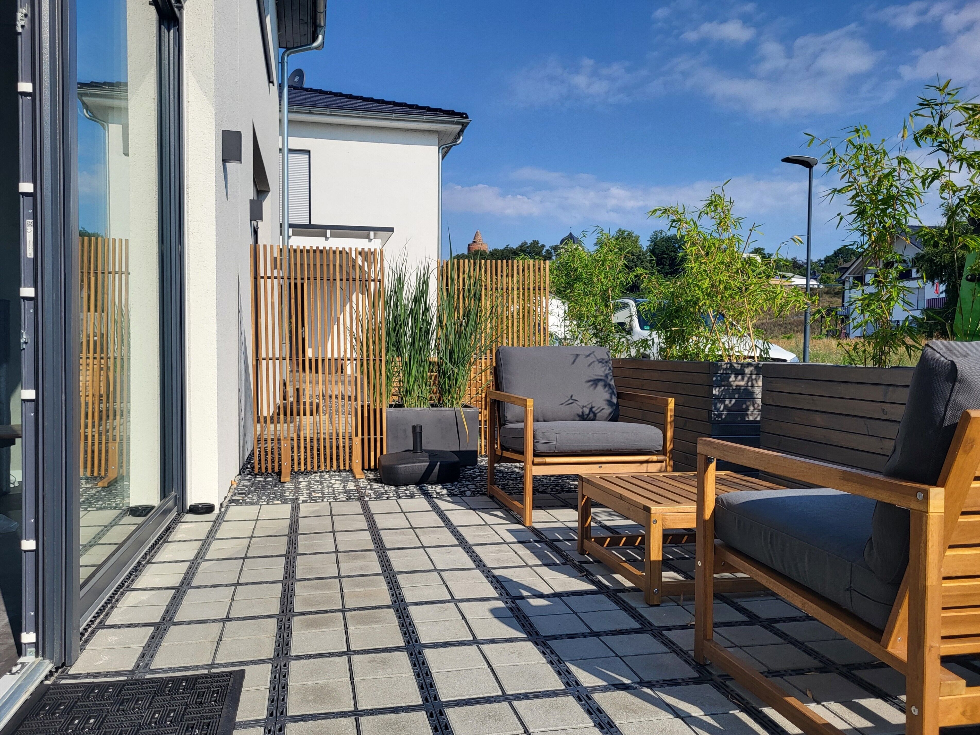 Un patio con un banco de madera, una silla y una pequeña mesa.
