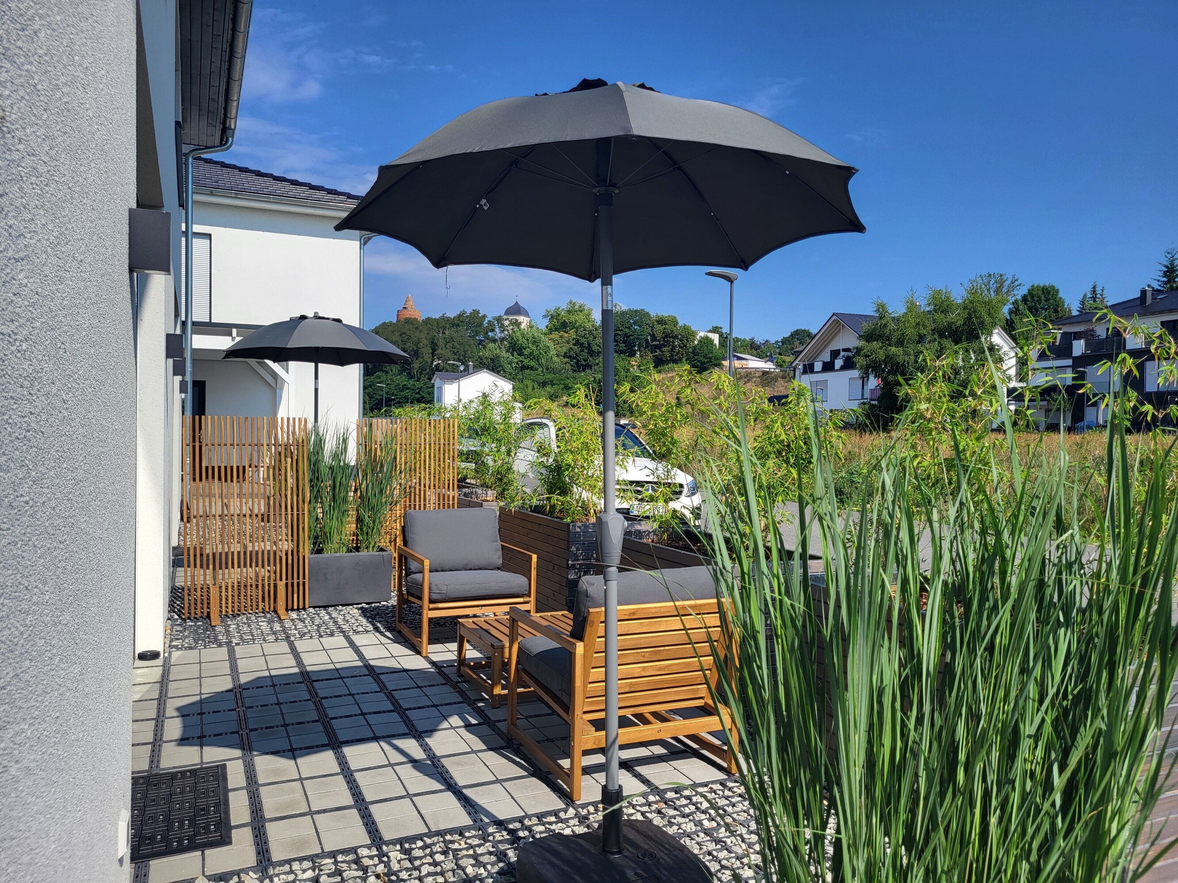 A patio with outdoor furniture, a large umbrella, and a view of the surrounding neighborhood.