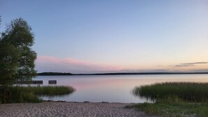 Ein sandiger Strand mit einem ruhigen See, einer Anlegestelle und grünen Flächen.