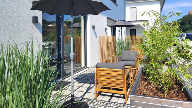 Eine Terrasse mit Gartenmöbeln, zwei Sonnenschirmen und einem Holzzaun.