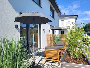 Un patio con mobiliario exterior, dos sombrillas y una valla de madera.