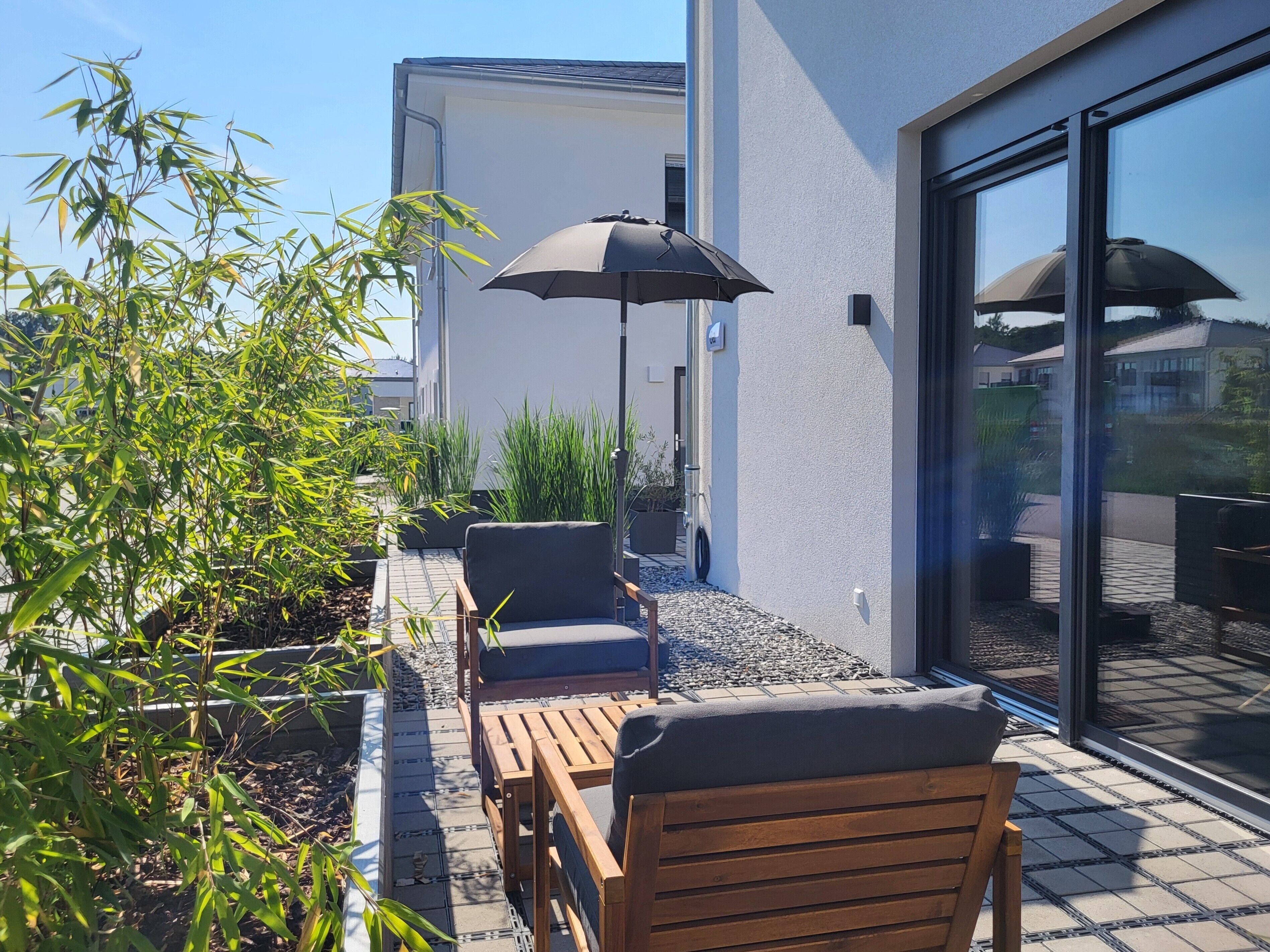 A patio with outdoor furniture, a black umbrella, and a building with a glass door.