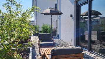 A patio with outdoor furniture, a black umbrella, and a building with a glass door.