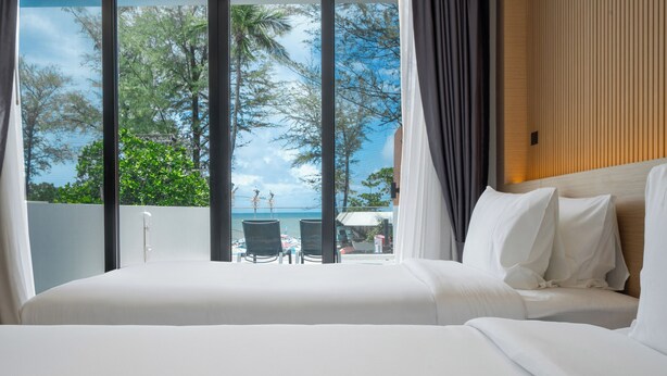 Ett hotellrum med en stor säng, utsikt över stranden och en balkong med stolar.