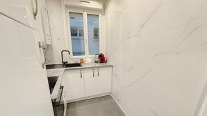 A compact kitchen with white cabinets, a window, and a sink. - Elegant Paris 11 Apartment, Near Metro & Dining (Paris)