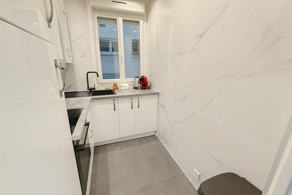 A compact kitchen with white cabinets, a window, and a sink.