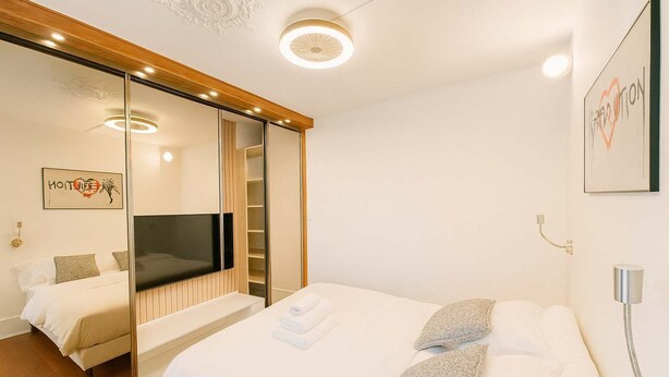 Une chambre d’hôtel moderne dotée d’un grand lit, d’une télévision, d’une armoire avec un miroir et d’une œuvre d’art accrochée au mur.