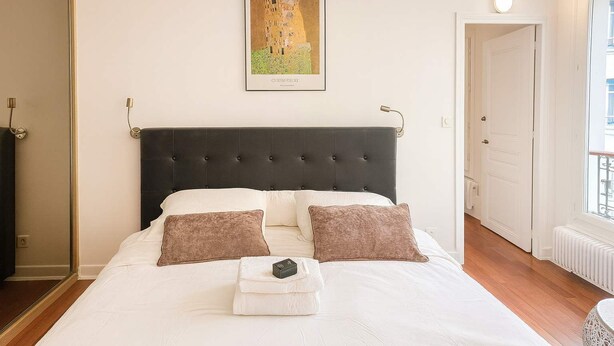 A neatly made bed with a dark headboard, two pillows, and a folded towel. - Elegant Paris 11 Apartment, Near Metro & Dining (Paris)