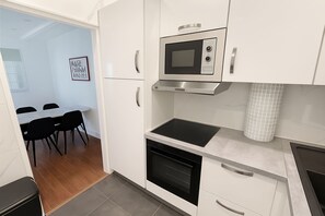 A modern kitchen with white cabinets, a built-in microwave, a stove, and a dining area with a table and chairs.