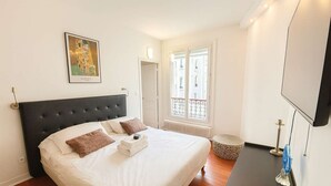 A hotel room with a large bed, a painting on the wall, a window with a view, and a bedside table with a lamp. - Elegant Paris 11 Apartment, Near Metro & Dining (Paris)