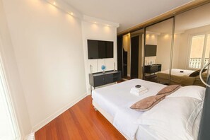 A modern hotel room with a large bed, a bedside table with a lamp, a flat-screen TV mounted on the wall, and a sliding door closet. - Elegant Paris 11 Apartment, Near Metro & Dining (Paris)