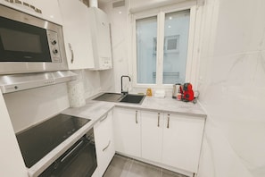 A compact kitchen with a microwave, oven, sink, and a window.