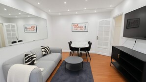 A modern living room with a grey sofa, a round coffee table, a TV, and a dining area with chairs and a table. - Elegant Paris 11 Apartment, Near Metro & Dining (Paris)