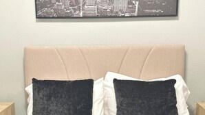Ein Bett mit einem beige bezogenen Kopfteil, zwei dunklen Kissen und weißen Bettwäsche.