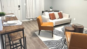 Ein modernes Wohnzimmer mit einem Holzesstisch, einem Ledersessel, einer Couch mit gemusterten Kissen und einem Zebra-Teppich.