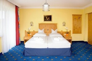 Uma cama de casal com roupa de cama branca, uma cabeceira de madeira, duas mesas de cabeceira com abajures e um quadro na parede.