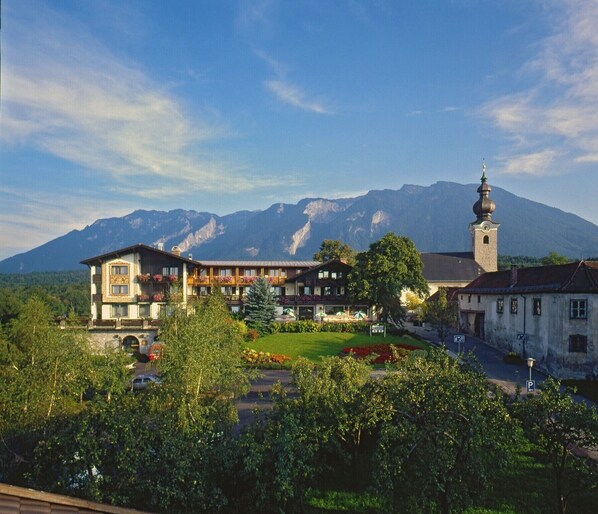 Hotel com montanhas ao fundo, destacando uma torre de igreja e vegetação exuberante.