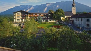 A hotel with a mountain backdrop, featuring a prominent church tower and lush greenery. - Apartment Römerstraße 64-persons, 40sqm, 1 bedroom, balcony or terrace (Bad Reichenhall)