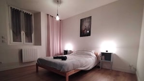A bedroom with a wooden bed, two bedside tables, a radiator, a window with curtains, and a painting on the wall. - "Le Nid Dauphinois" fully equipped - Ideal for business, couples & families! (L'Albenc)